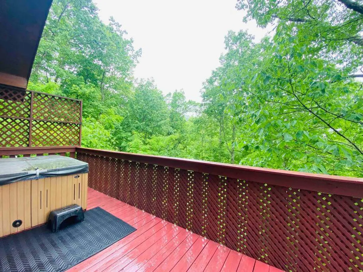 A serene wooden deck featuring a bubbling hot tub surrounded by lush greenery. The space is perfect for relaxing and soaking in the peaceful mountain atmosphere, whether during the day or under the stars at night.