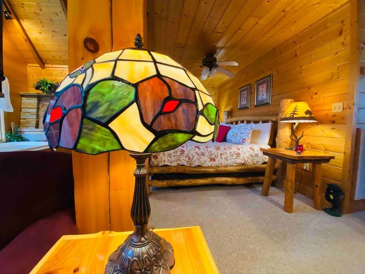 A cozy bedroom setting with a stained glass lamp casting a warm glow over a bed with floral bedding and classic wooden furniture, inviting quiet moments of reading or relaxation.