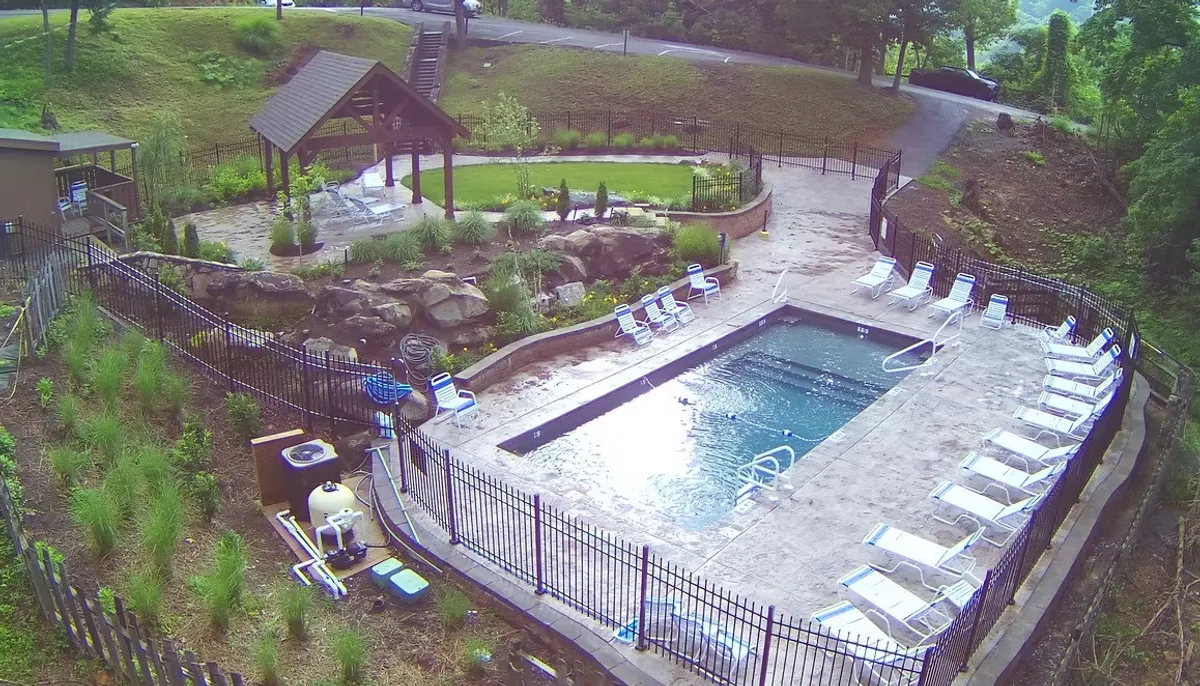 A beautifully landscaped swimming pool area with lounge chairs, a gazebo, and rock features. The scene is set for fun or relaxation, with ample space for swimming, sunbathing, or gathering with friends and family. The backdrop of natural landscaping adds to the sense of a luxurious, resort-like environment.