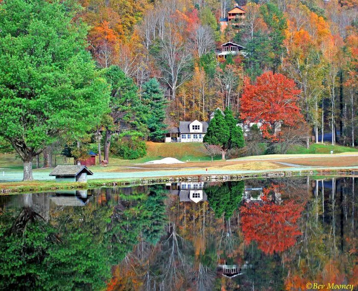 A peaceful scene with a reflective lake, colorful trees, grassy landscaping, and nearby houses. The setting is tranquil and showcases the natural beauty of the area, ideal for outdoor activities and relaxation.