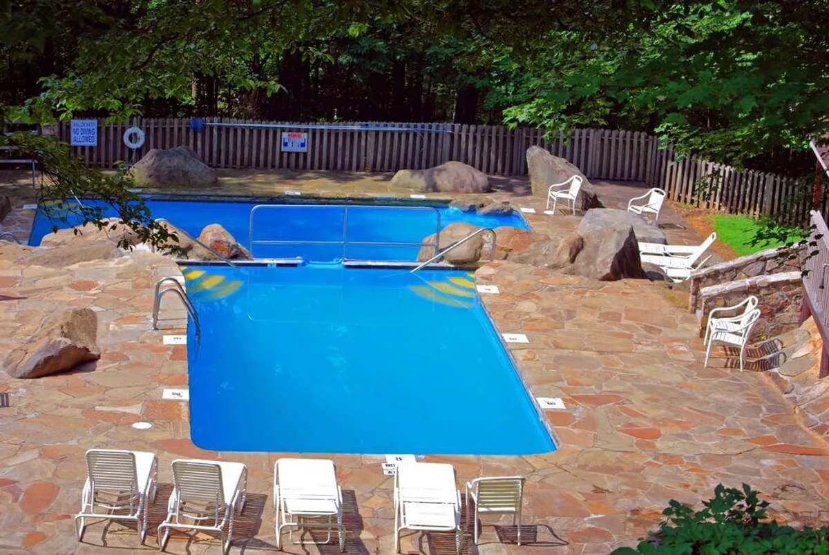 This exterior image showcases a sparkling swimming pool surrounded by natural rock formations and comfortable lounge chairs. The inviting setting is ideal for families and friends to swim, relax, and socialize during warm seasons.