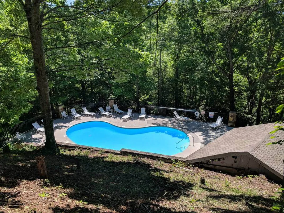 This image features a sparkling swimming pool surrounded by trees and a patio area dotted with lounge chairs. The inviting blue water and serene setting evoke a relaxed, resort-like atmosphere, ideal for unwinding or socializing. The surrounding greenery enhances the sense of a peaceful mountain retreat.
