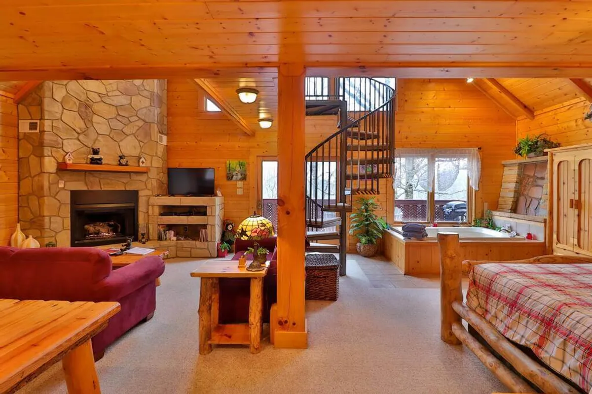This image showcases a warm, inviting living area featuring a prominent stone fireplace, spiral staircase, wooden furniture, and expansive windows that let in natural light. The cozy seating area is ideal for snuggling up together and enhancing the romantic ambiance described in the section.